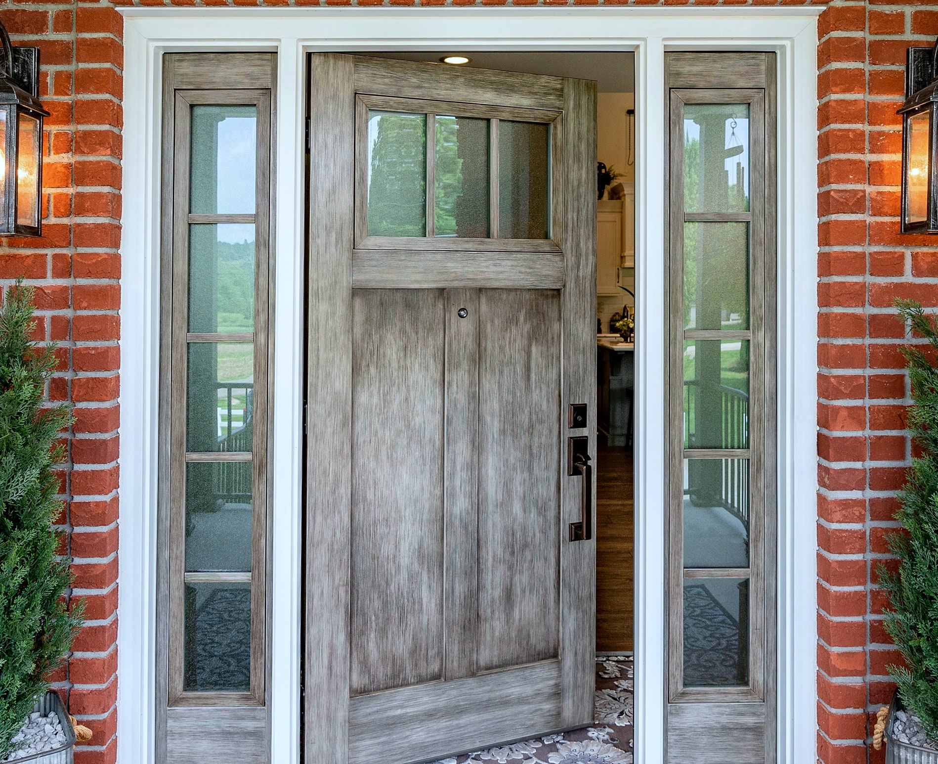 Gray wood-grain entry door with sidelights in red brick wall