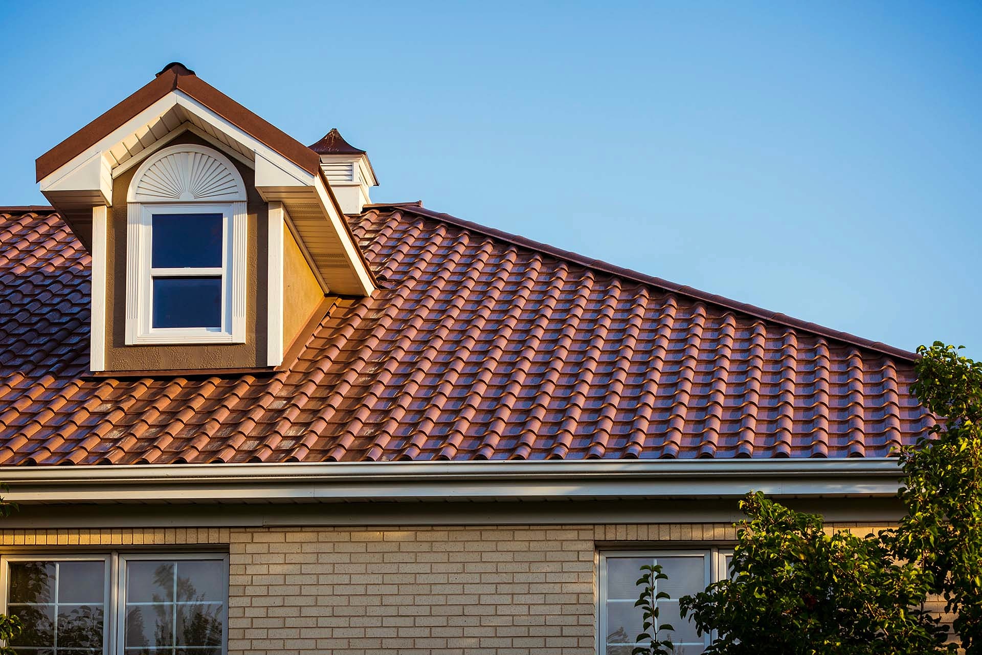 Red tile-style metal roof with dormer on brick house